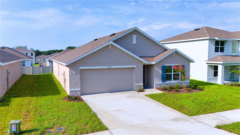 A single-story suburban house with a tan exterior, a two-car garage, and a concrete driveway — 7230 SE 112TH LANE, BELLEVIEW, FL