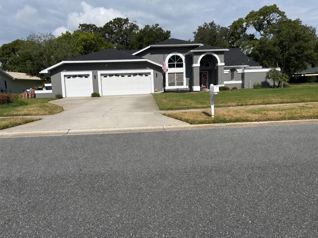 A gray single-story house with a two-car garage, arched entryway, and a paved driveway — 18561 WINDING OAKS BOULEVARD, HUDSON, FL