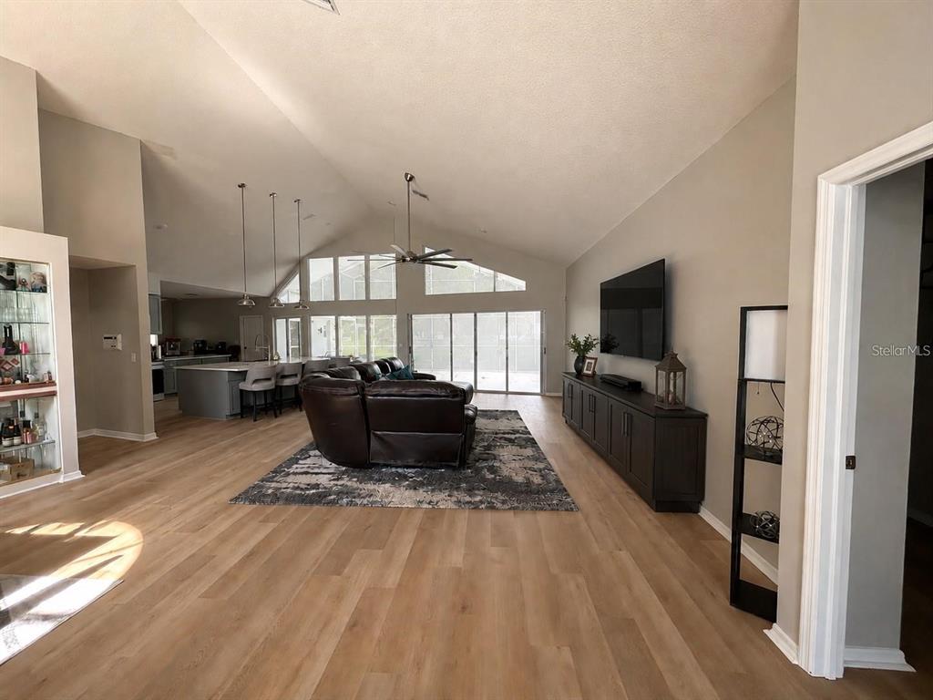 A spacious open-concept living room features light wood flooring, a vaulted ceiling, and a kitchen — 18561 WINDING OAKS BOULEVARD, HUDSON, FL