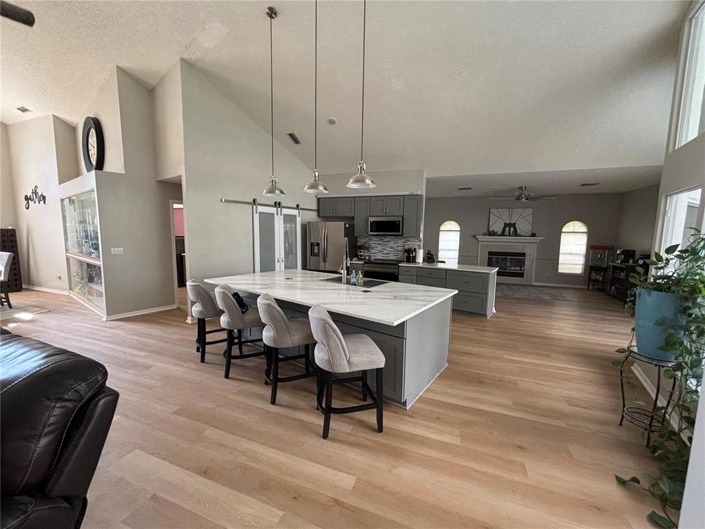 An open-concept kitchen features a large marble-topped island, gray cabinetry, and light wood flooring — 18561 WINDING OAKS BOULEVARD, HUDSON, FL