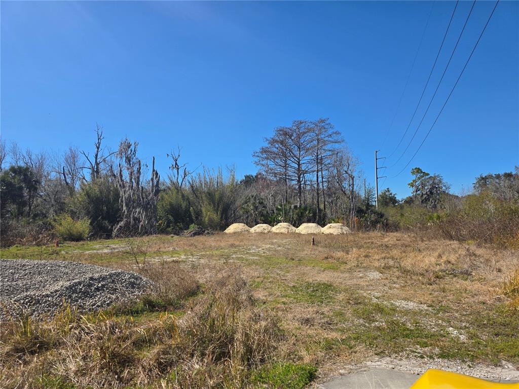 A vacant, grassy lot features piles of sand and trees under a clear blue sky — 470 N STATE ROAD 415, OSTEEN, FL