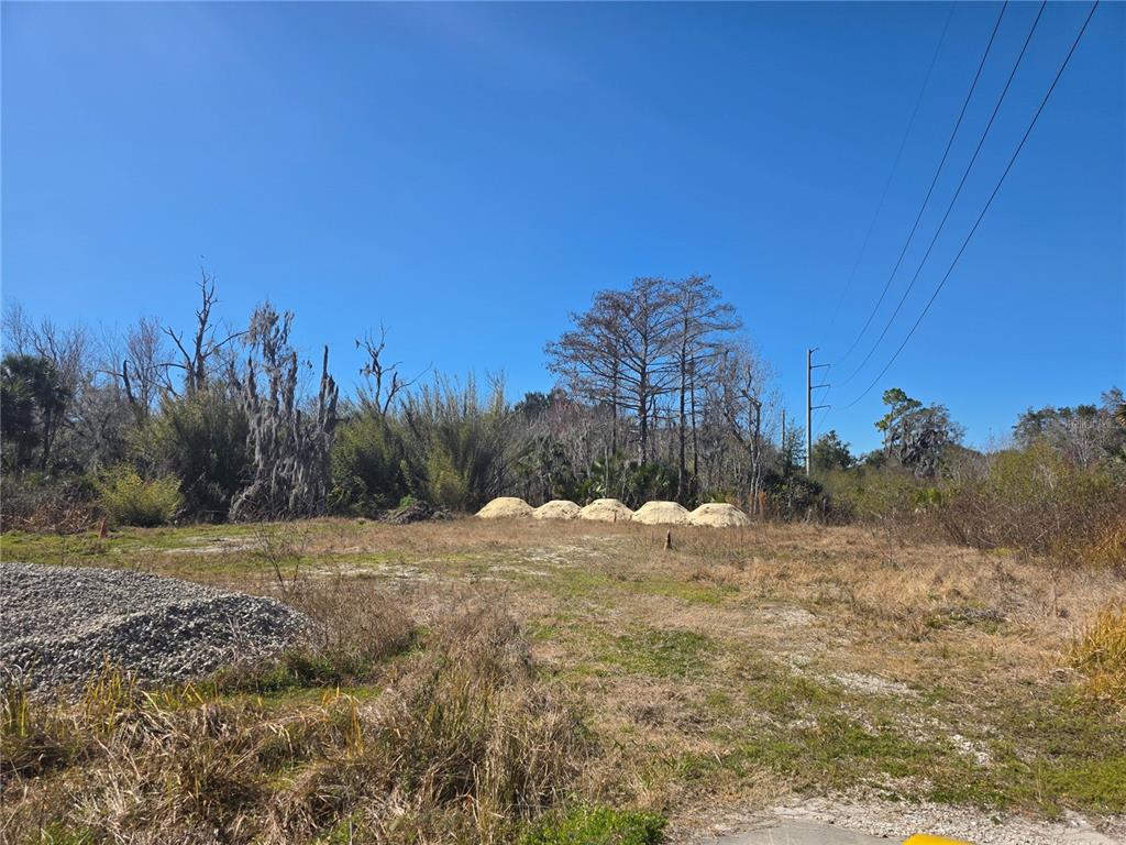 A vacant, grassy lot features piles of sand and gravel with trees in the background — 470 N STATE ROAD 415, OSTEEN, FL