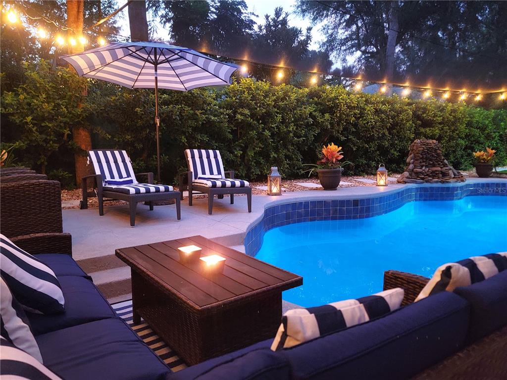 A backyard patio features a swimming pool, lounge chairs, and outdoor seating under string lights — 9800 SW 190TH TERRACE ROAD, DUNNELLON, FL