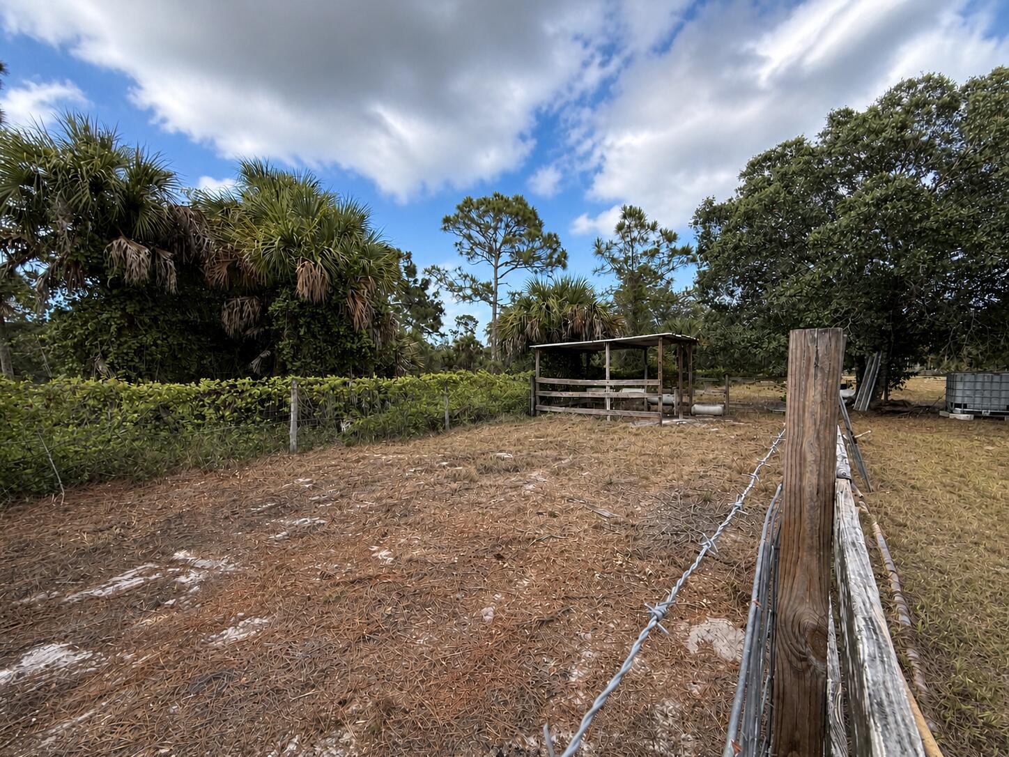 A fenced dirt pasture features a small wooden animal shelter under a cloudy blue sky — 825 S Verda Street, Clewiston FL 33440, CLEWISTON, FL