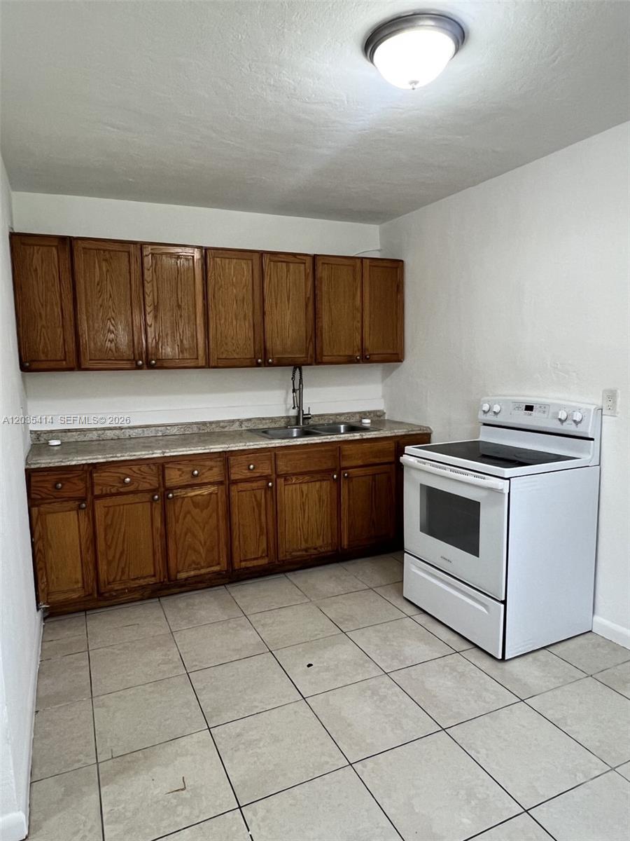 A kitchen features wood cabinets, a laminate countertop, a white stove, and tiled flooring — 1754 NW 45th St # 1754, Miami FL 33142, MIAMI, FL