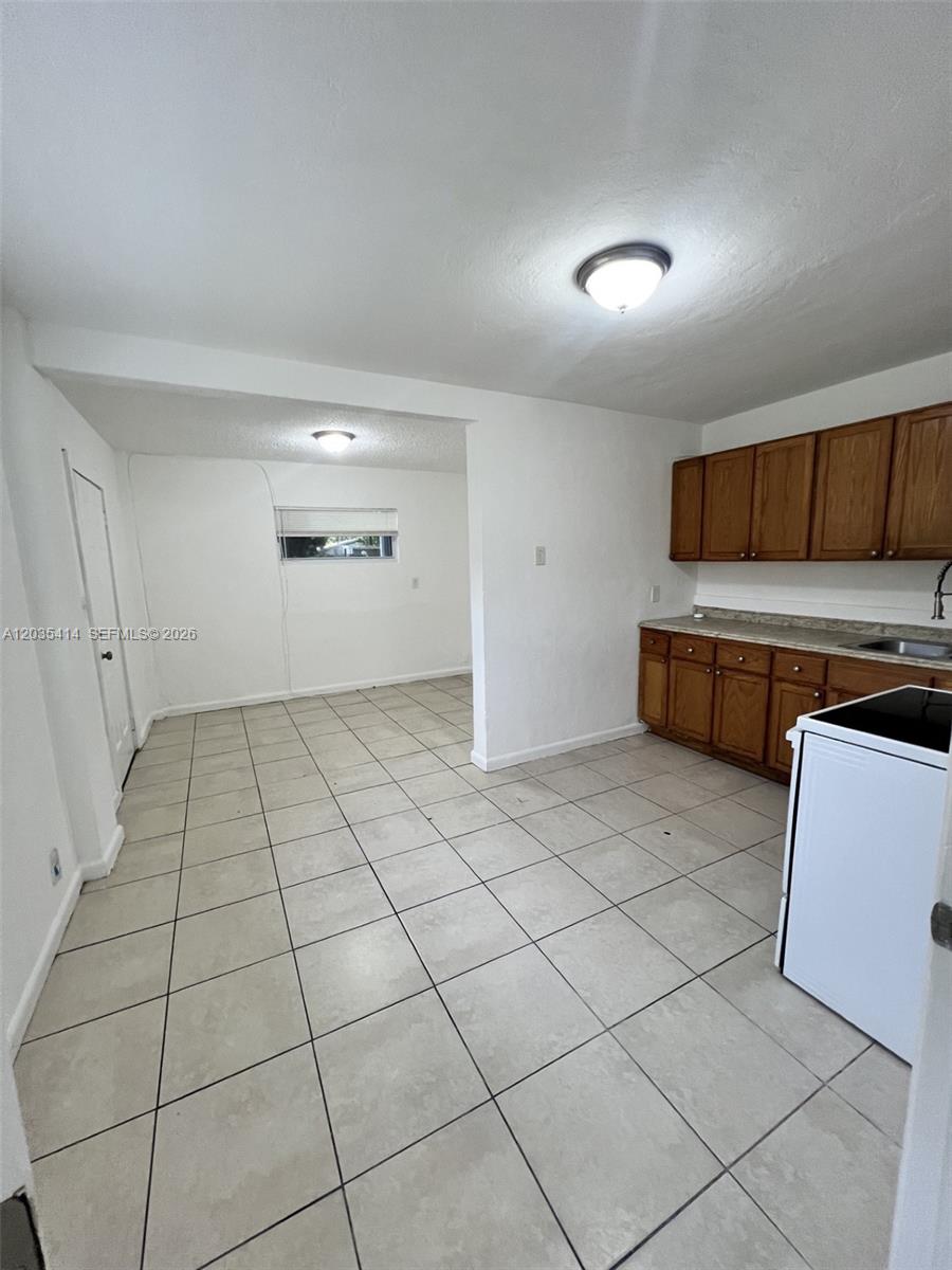 A kitchen with wooden cabinets and tiled floors opens into an adjacent living area — 1754 NW 45th St # 1754, Miami FL 33142, MIAMI, FL