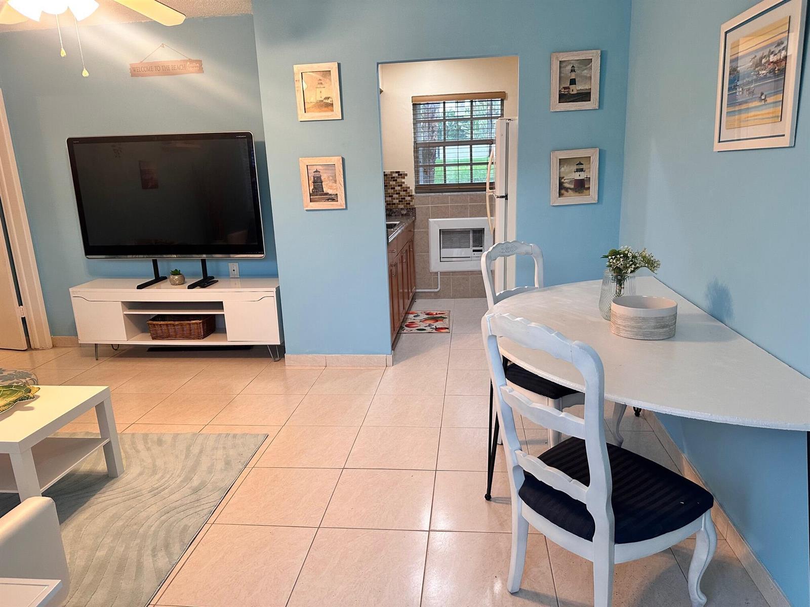 A living room with light blue walls, tile flooring, a television, and a dining area — 3240 NE 16th Street # 7, Pompano Beach FL 33062, POMPANO BEACH, FL