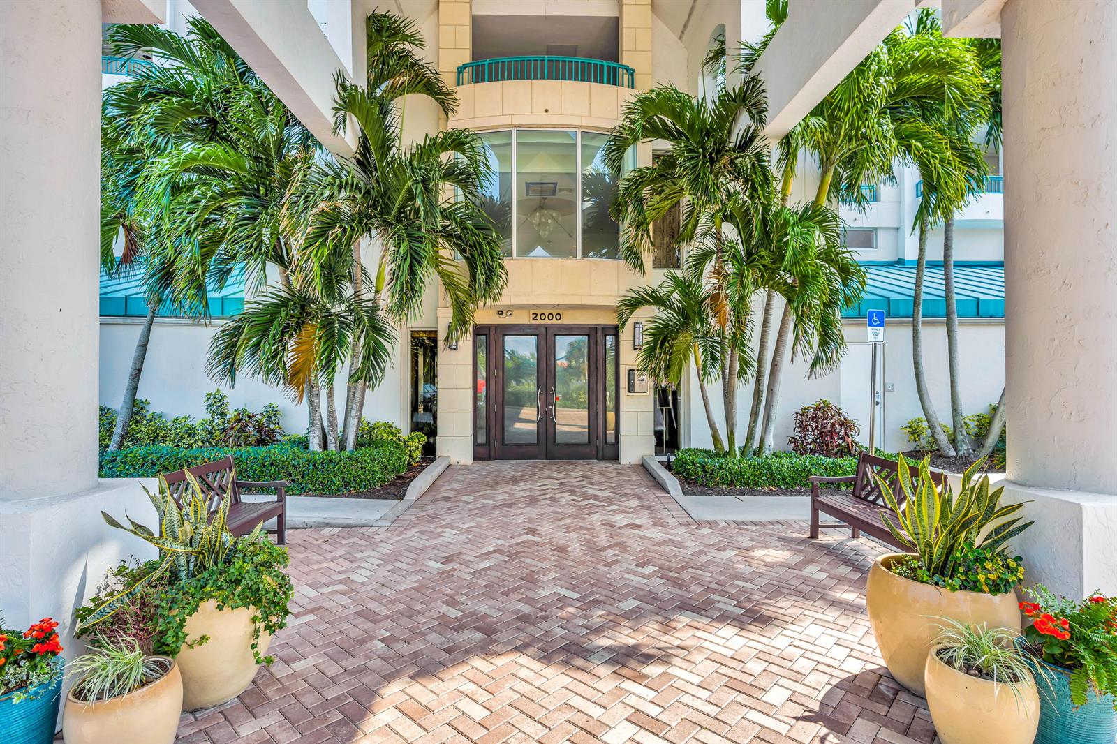 The exterior entrance of a building features a brick walkway, palm trees, and benches — 2000 S Highway A1a # 603, Jupiter FL 33477, JUPITER, FL