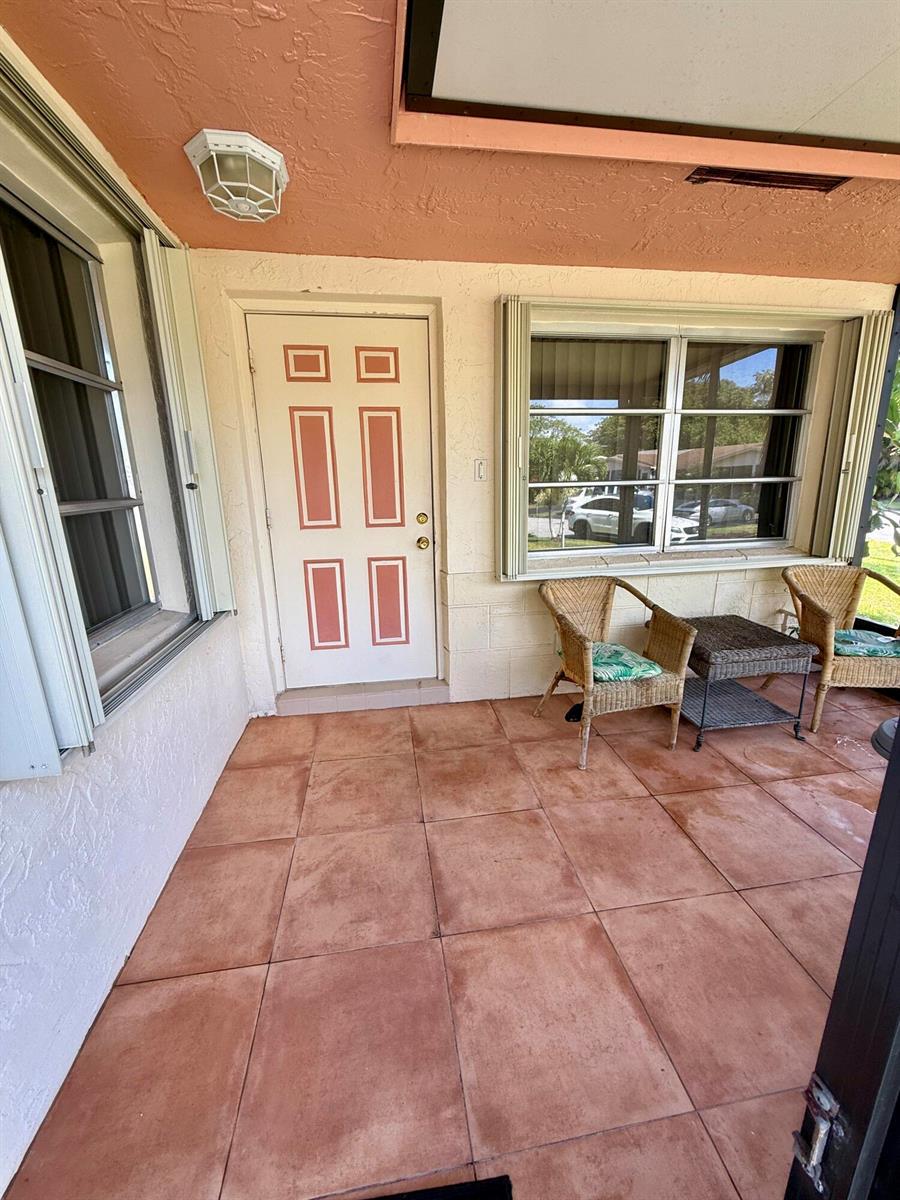 A covered porch features terracotta-colored floor tiles, a white door, and two wicker chairs — 14464 Campanelli Drive, Delray Beach FL 33484, DELRAY BEACH, FL