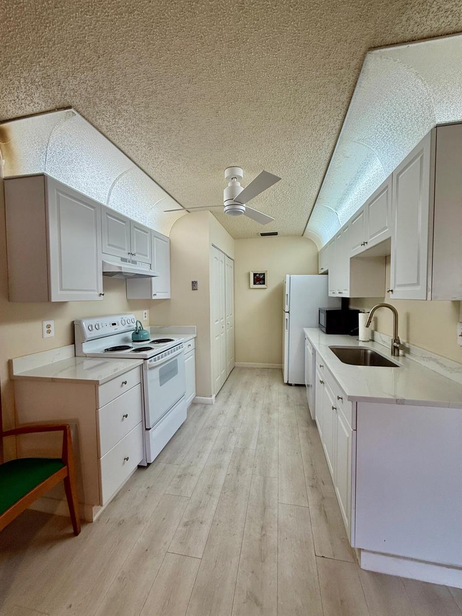 A galley kitchen features white cabinets, light countertops, stainless steel sink, and wood-look flooring — 14464 Campanelli Drive, Delray Beach FL 33484, DELRAY BEACH, FL
