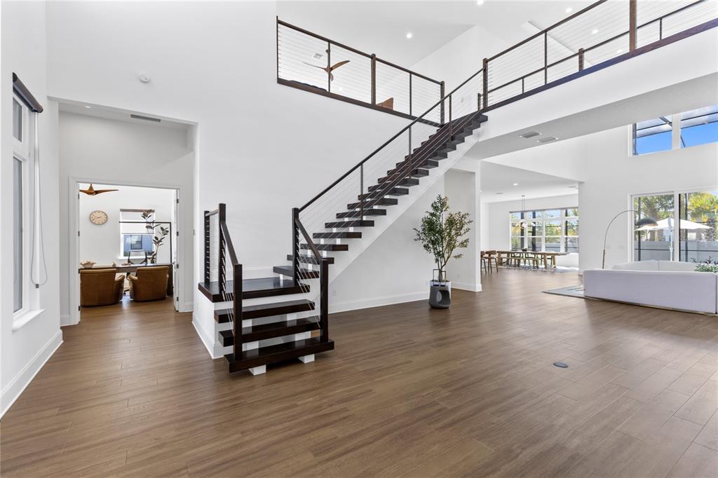 A modern living area features a dark wood staircase with cable railings and hardwood flooring — 9076 SANTORINI DRIVE, ORLANDO, FL