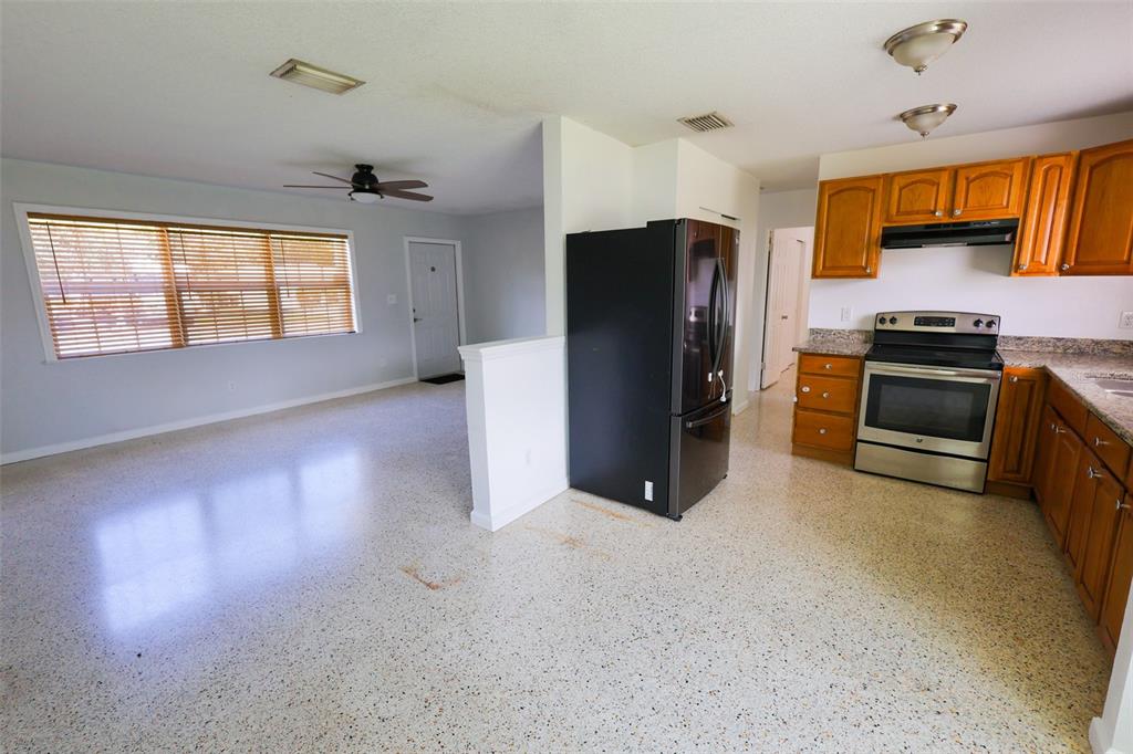 An open-concept kitchen and living area featuring terrazzo flooring, wooden cabinets, and stainless steel appliances — 8300 57TH STREET N, PINELLAS PARK, FL