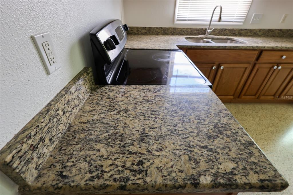 A kitchen features granite countertops, a black electric stove, and wood cabinets — 8300 57TH STREET N, PINELLAS PARK, FL