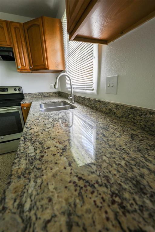 A kitchen features granite countertops, a stainless steel sink, and wooden cabinets above a stove — 8300 57TH STREET N, PINELLAS PARK, FL