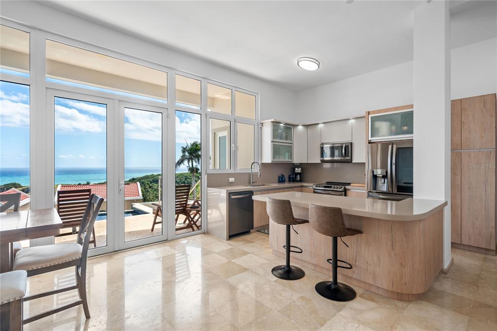 A modern kitchen with a breakfast bar, light wood cabinetry, and floor-to-ceiling ocean view windows — 1 CALLE UNIT 78, HUMACAO, PR
