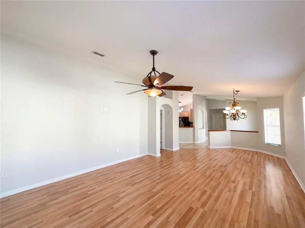 A spacious living area with light wood flooring, a ceiling fan, and a dining chandelier — 396 GRAND CANAL DRIVE, KISSIMMEE, FL