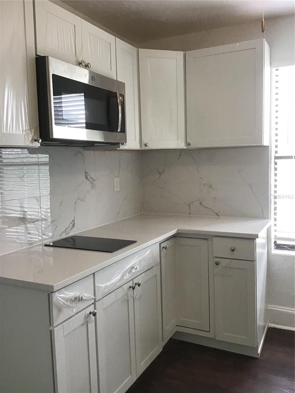 A kitchen features white cabinets, a stainless steel microwave, and white marble-patterned backsplash tiles — 401 COLONIA LANE E UNIT 15, NOKOMIS, FL