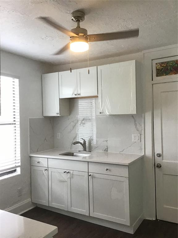 A kitchen features white cabinets, a marble-look backsplash, a stainless steel sink, and a ceiling fan — 401 COLONIA LANE E UNIT 15, NOKOMIS, FL