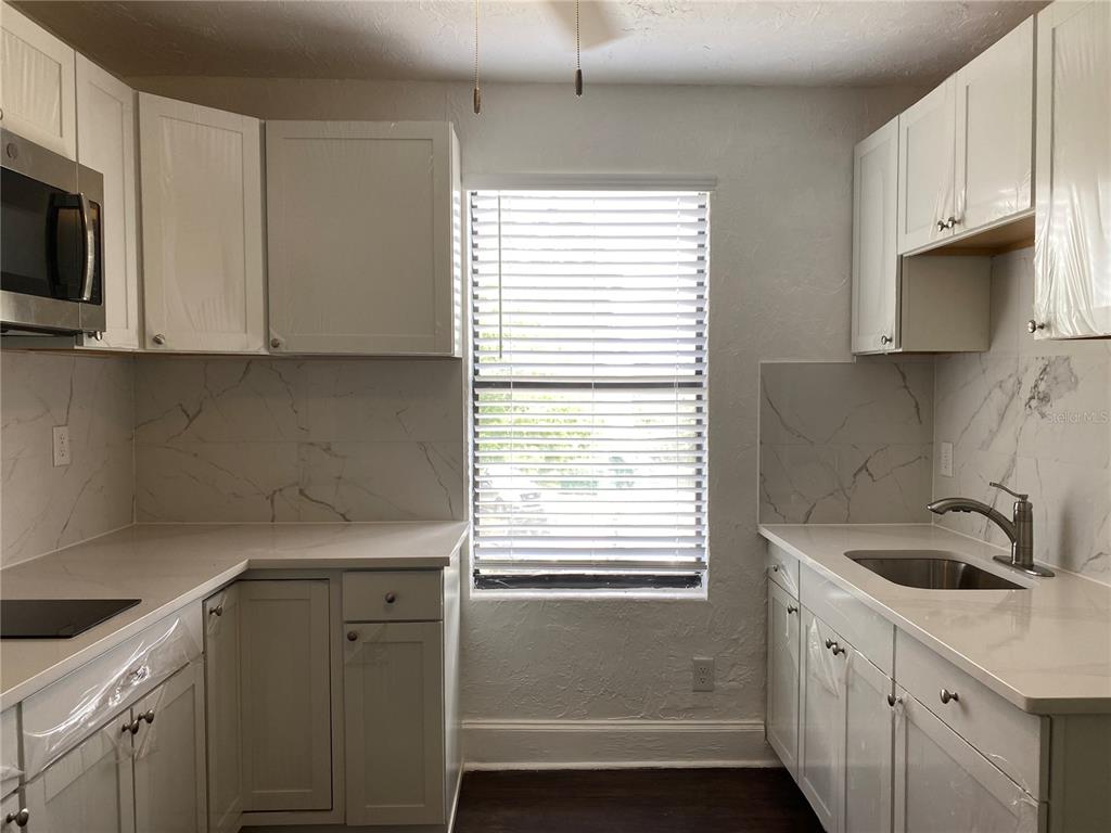 A kitchen features white cabinets, marble-look backsplash, light countertops, and a window with blinds — 401 COLONIA LANE E UNIT 15, NOKOMIS, FL