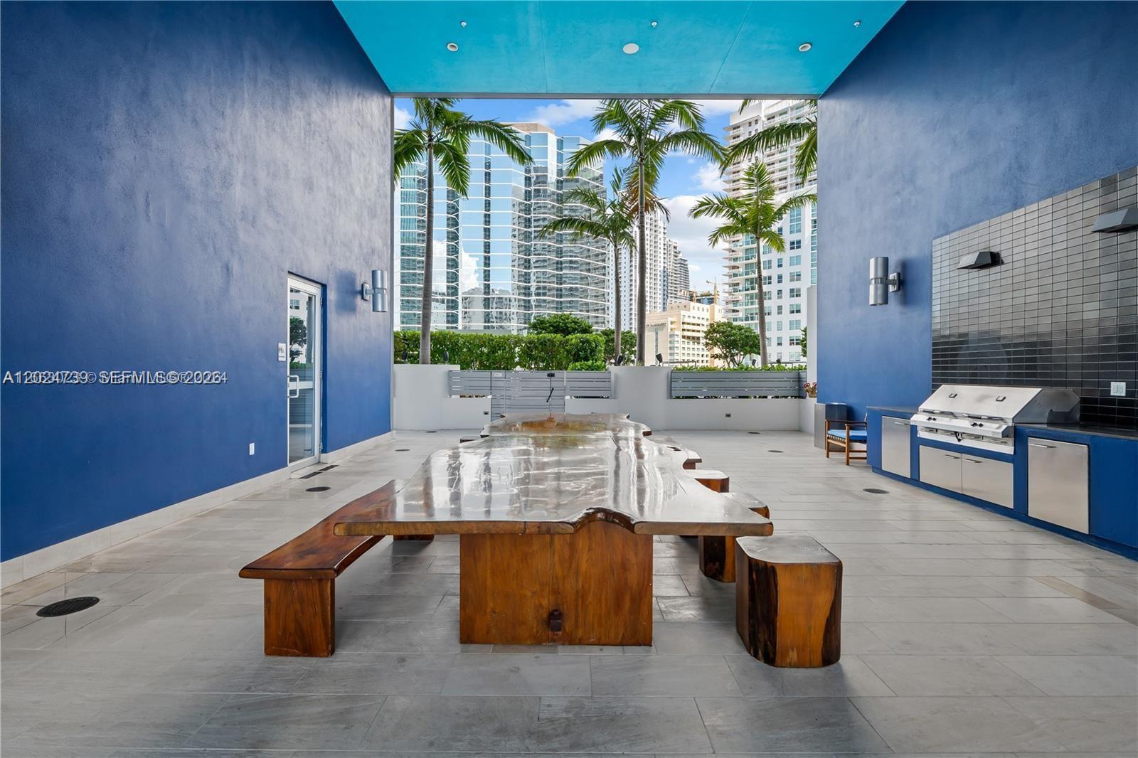 An outdoor dining area features a large wooden table, benches, and a built-in grill station — 1300 Brickell Bay Dr # 1007, Miami FL 33131, MIAMI, FL