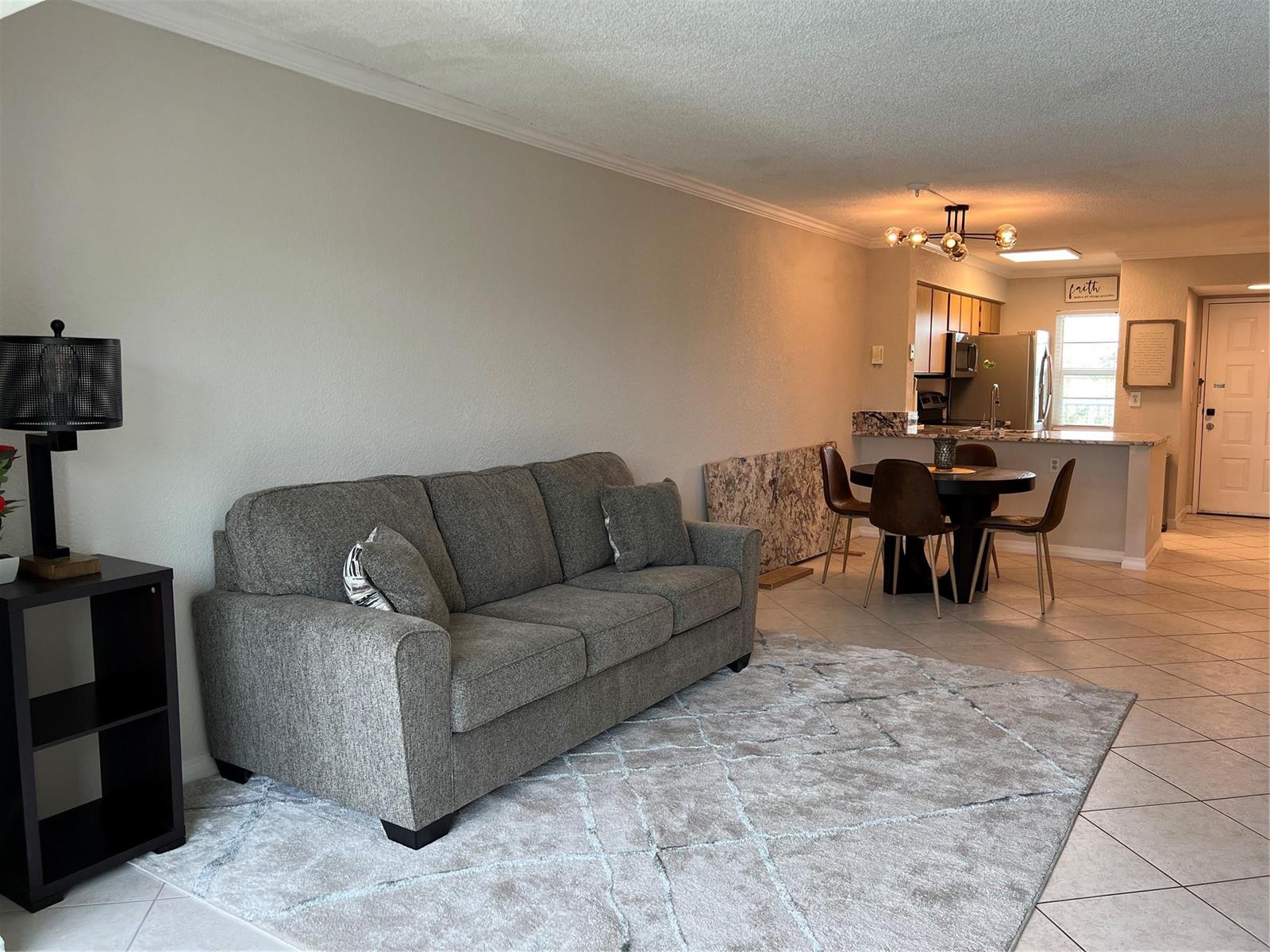 A living room with a grey sofa, area rug, and an adjacent dining area — 2220 N Cypress Bend Drive # 301, Pompano Beach FL 33069, POMPANO BEACH, FL