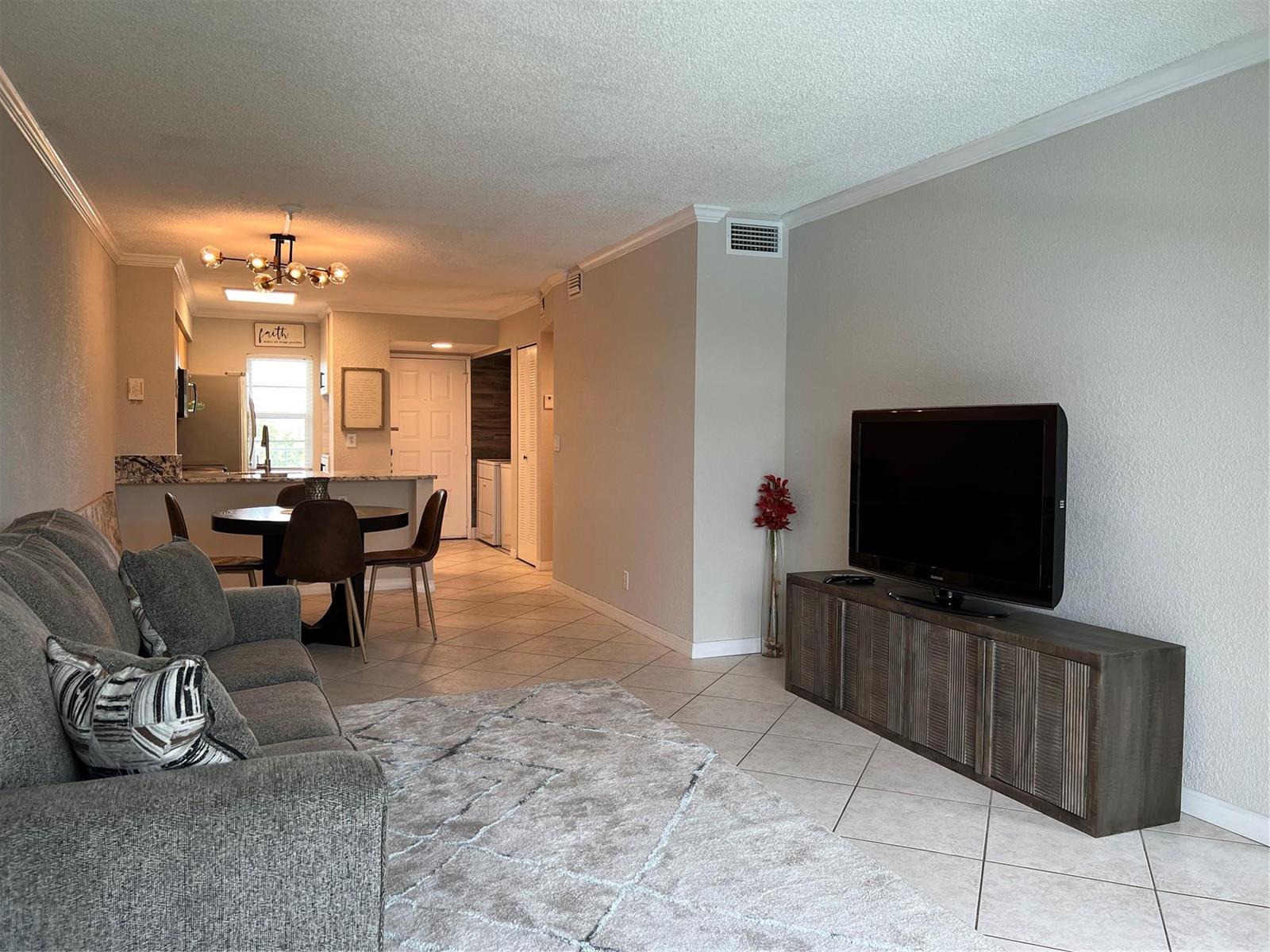 A living room with tile flooring, a gray sofa, and a television on a wooden console — 2220 N Cypress Bend Drive # 301, Pompano Beach FL 33069, POMPANO BEACH, FL