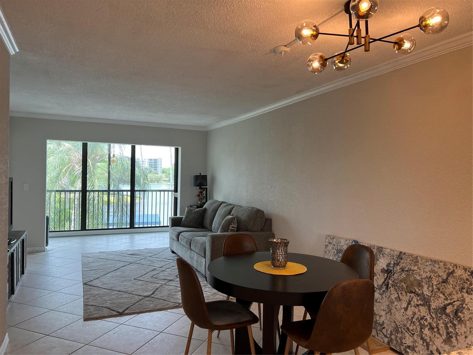 A living and dining area features a grey sofa, round table, and a balcony view — 2220 N Cypress Bend Drive # 301, Pompano Beach FL 33069, POMPANO BEACH, FL
