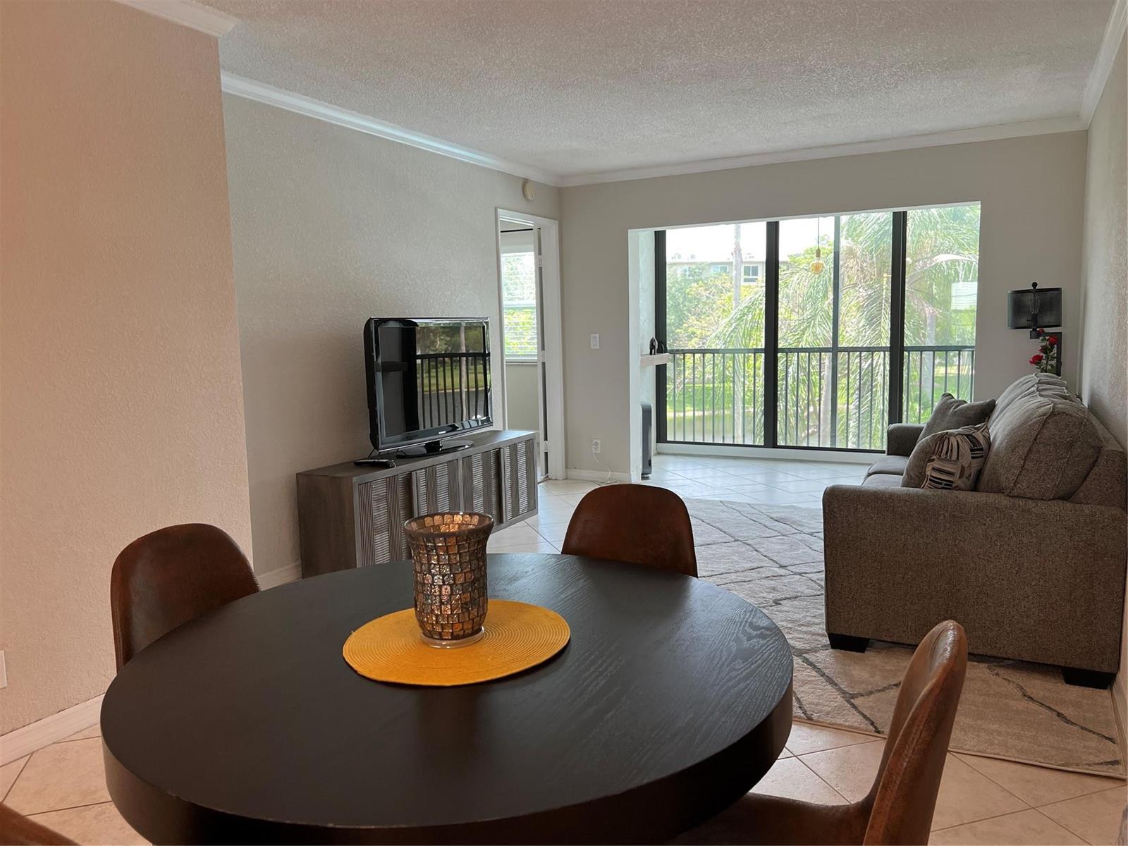 A dining area with a round table overlooks a living room with a balcony view — 2220 N Cypress Bend Drive # 301, Pompano Beach FL 33069, POMPANO BEACH, FL