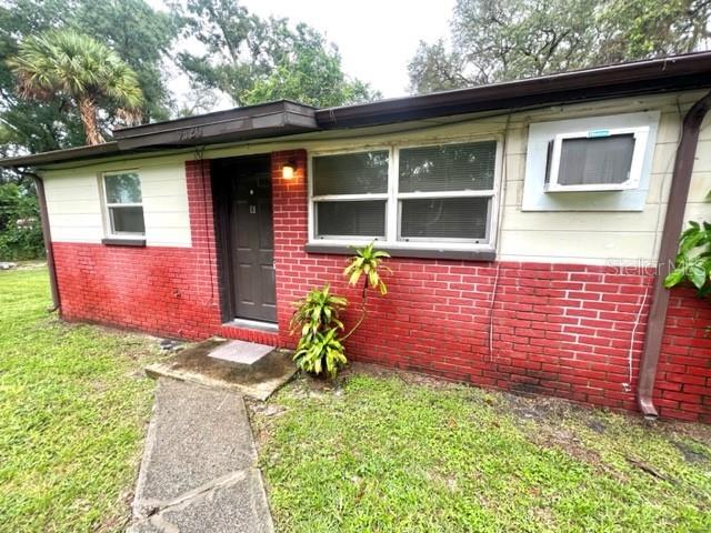 A single-story house features red brick siding, a dark front door, and a window air conditioner — 9418 GREYSTONE ROAD, THONOTOSASSA, FL