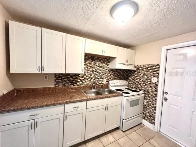 A kitchen features white cabinets, a brown countertop, a tiled backsplash, and a white stove — 9418 GREYSTONE ROAD, THONOTOSASSA, FL