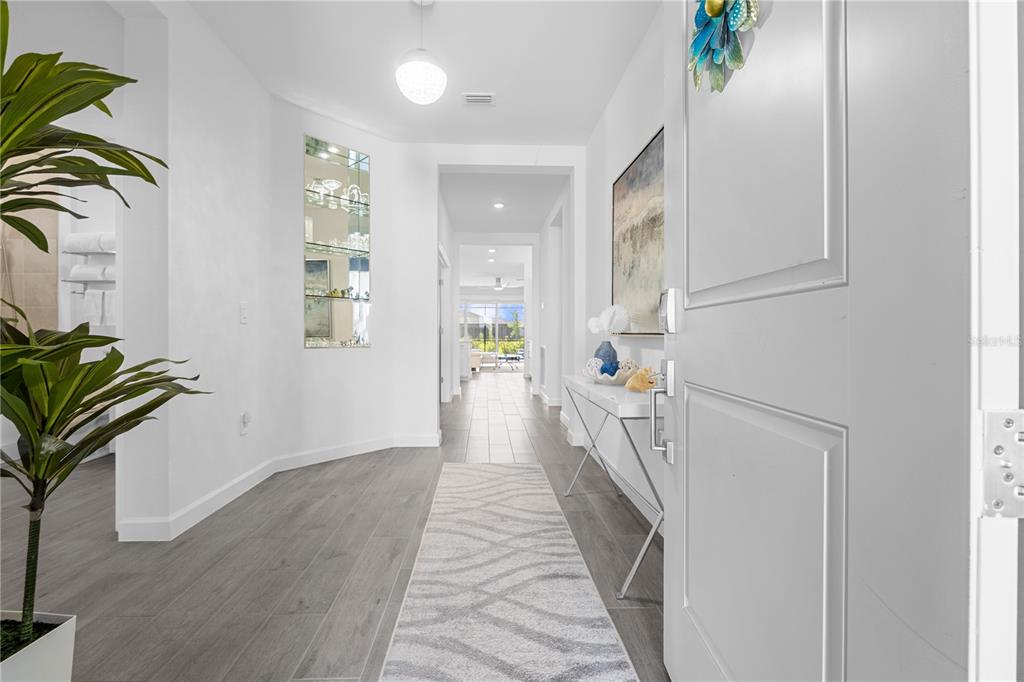 A bright entryway features gray wood-look tile flooring, a runner rug, and a mirrored niche — 14964 WHITE PEARL ROAD, PUNTA GORDA, FL
