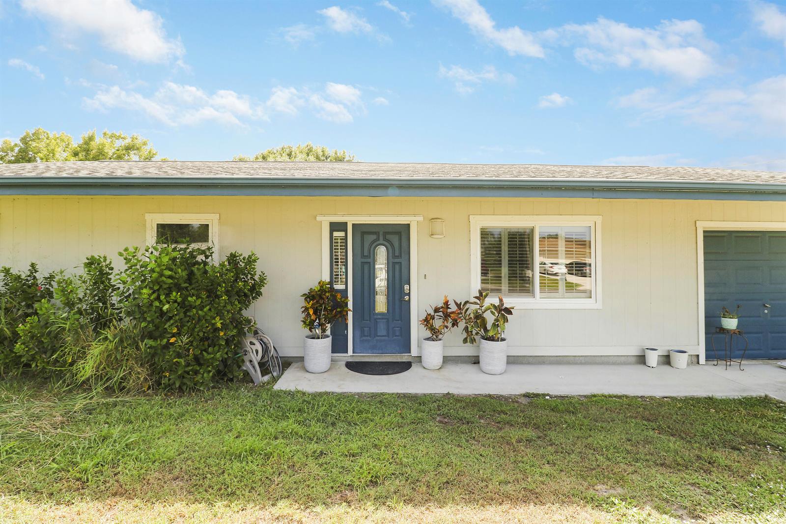 The exterior of a single-story house features light siding, a blue front door, and a garage — 5601 Palm Drive, Fort Pierce FL 34982, FORT PIERCE, FL