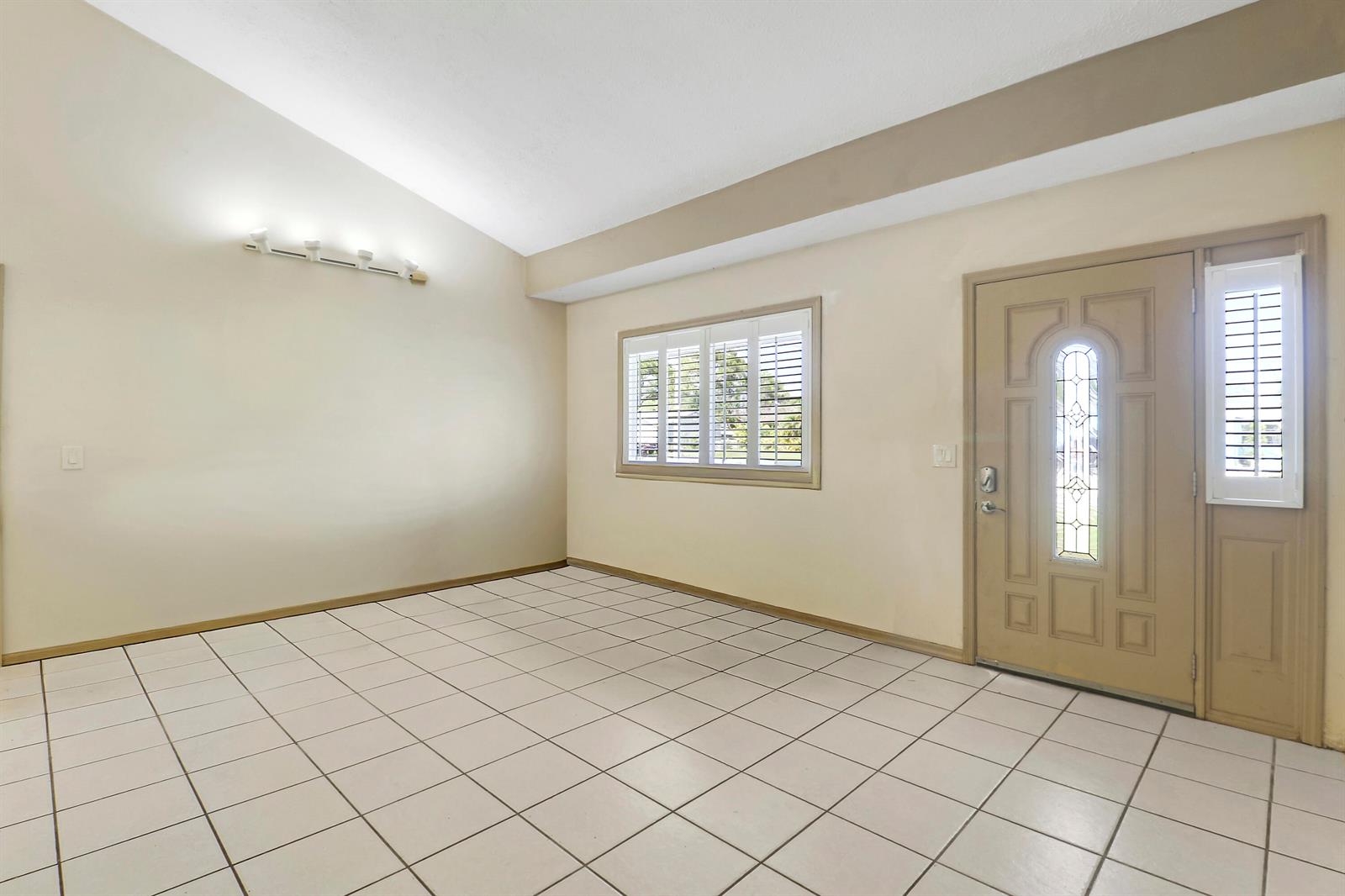An empty room with white tile flooring, a vaulted ceiling, and a beige front door — 5601 Palm Drive, Fort Pierce FL 34982, FORT PIERCE, FL