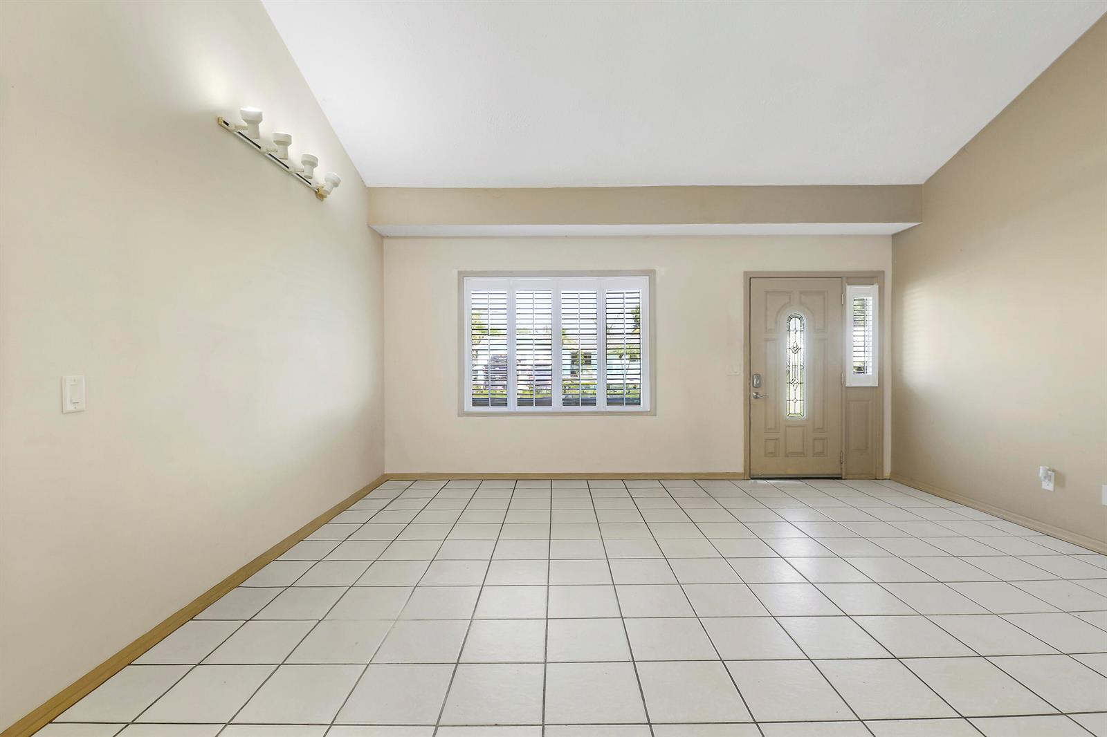 An empty room features white tile flooring, a vaulted ceiling, a window, and an entry door — 5601 Palm Drive, Fort Pierce FL 34982, FORT PIERCE, FL