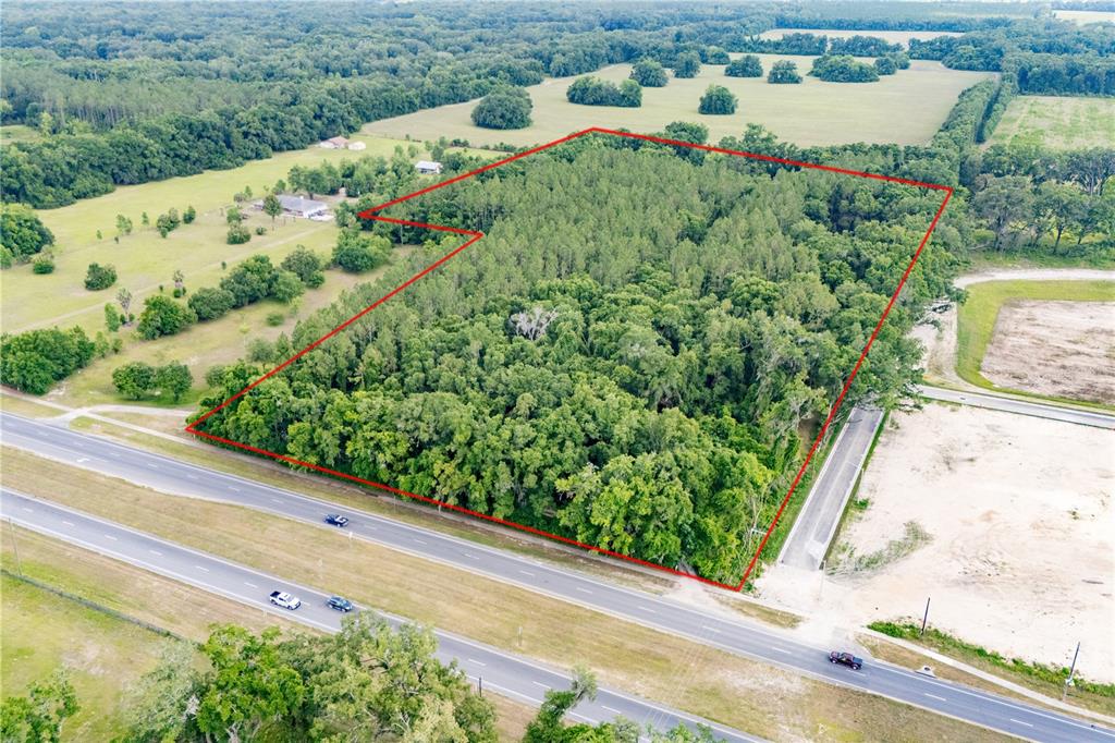 An aerial view shows a wooded plot of land outlined in red beside a highway — 23227 W NEWBERRY ROAD, NEWBERRY, FL