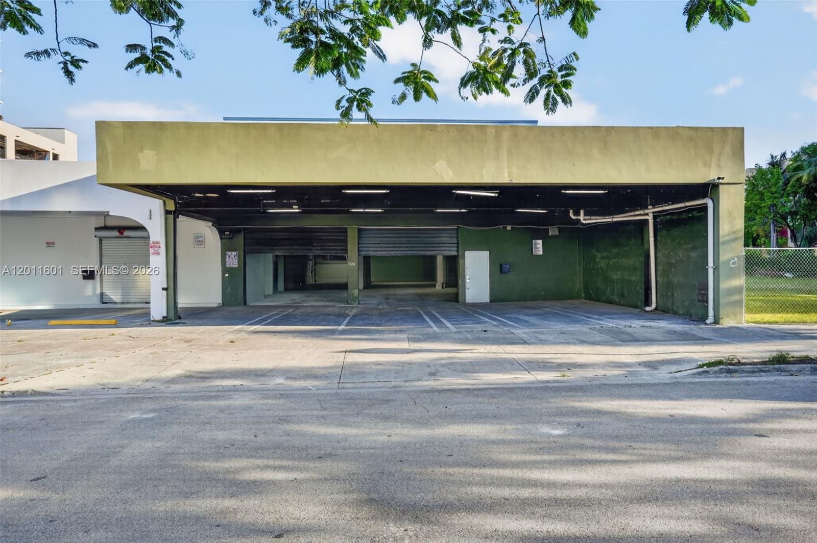 An exterior view of a commercial building with a covered parking area and roll-up doors — 500 W Flagler St, Miami FL 33130, MIAMI, FL
