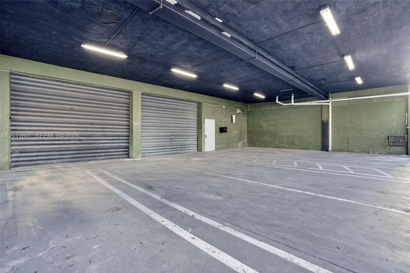 An indoor parking garage features two roll-up metal doors, concrete floors, and exposed ceiling lights — 500 W Flagler St, Miami FL 33130, MIAMI, FL