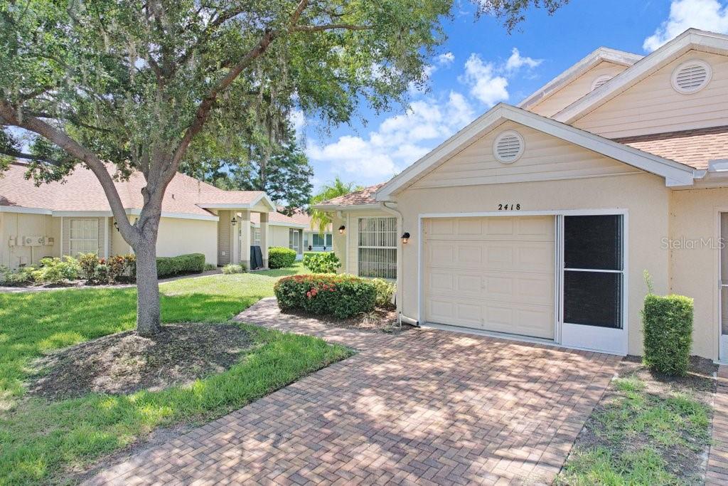 A single-story house with a brick driveway, a one-car garage, and a landscaped front yard — 2418 NEW HAVEN CIRCLE UNIT 83, SUN CITY CENTER, FL