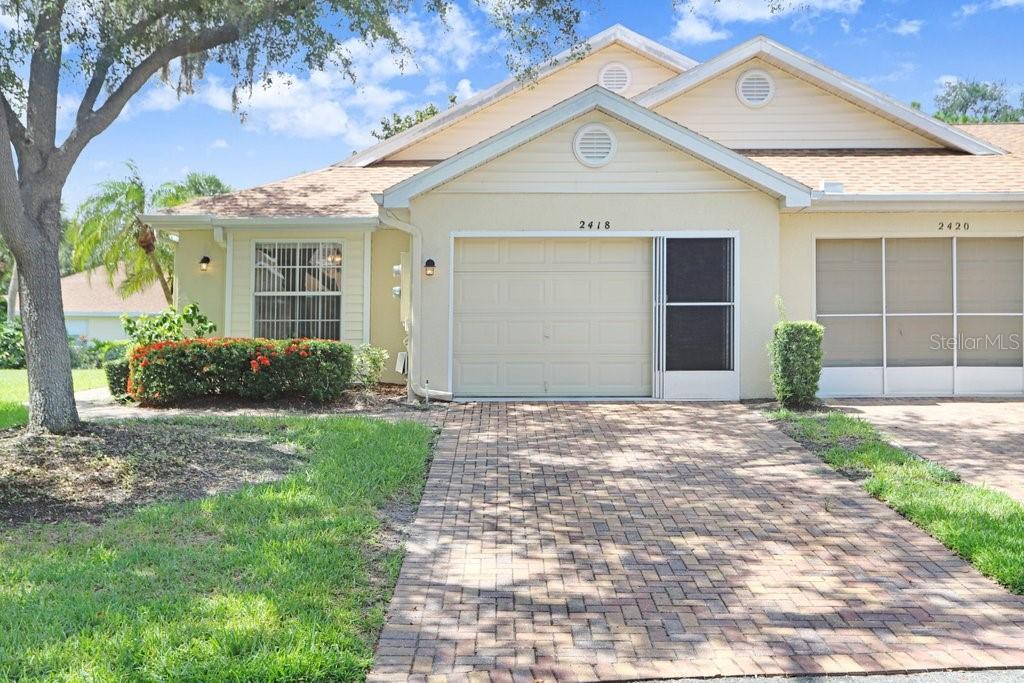 A tan duplex exterior features a brick paver driveway, a garage, and a front entrance — 2418 NEW HAVEN CIRCLE UNIT 83, SUN CITY CENTER, FL