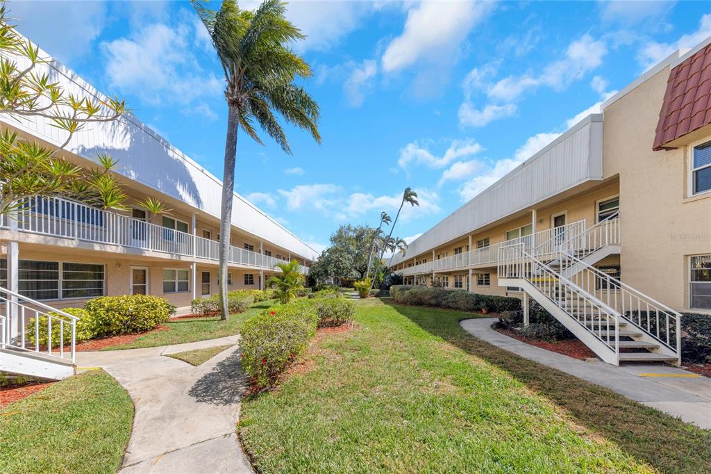 A courtyard between two multi-story apartment buildings with palm trees, walkways, and exterior staircases — 10032 65TH AVENUE N UNIT 9, ST PETERSBURG, FL
