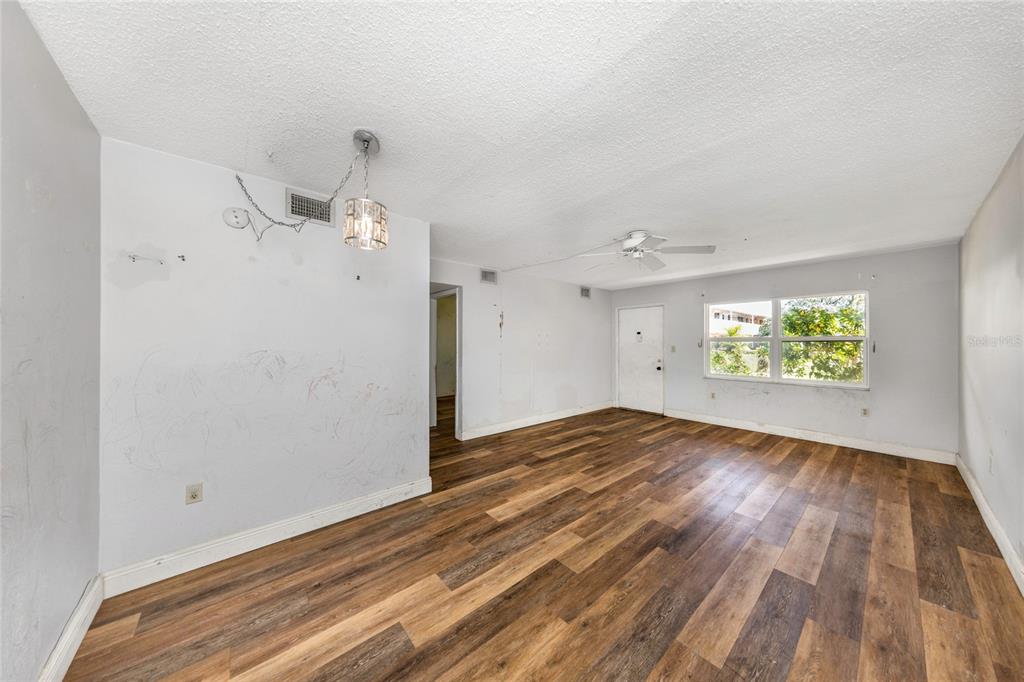 An empty living room with wood-look flooring, a ceiling fan, and a hanging light fixture — 10032 65TH AVENUE N UNIT 9, ST PETERSBURG, FL