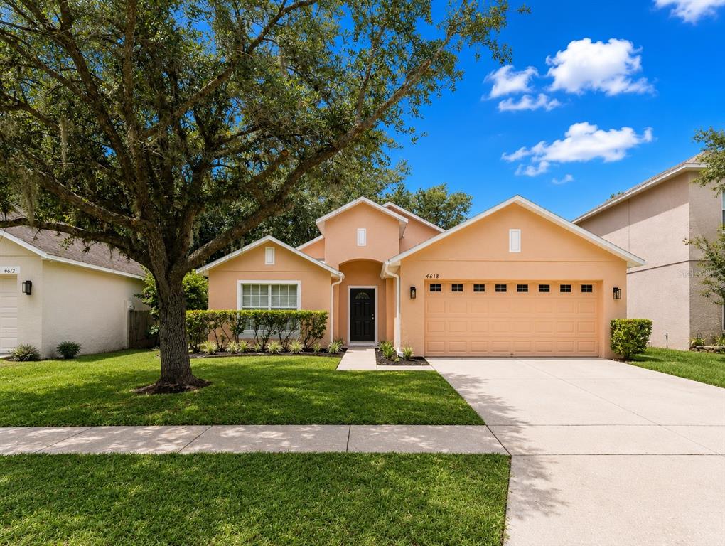 A single-story peach-colored house with a two-car garage and a large tree in front — 4618 AGUILA PLACE, ORLANDO, FL