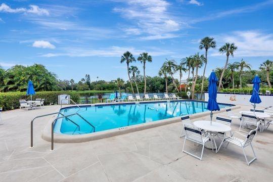 A swimming pool surrounded by a patio, lounge chairs, and palm trees under a blue sky — 220 BELLEVIEW BOULEVARD UNIT 203, BELLEAIR, FL