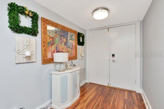 An entryway features a white cabinet, a framed painting, a wall sconce, and wood flooring — 220 BELLEVIEW BOULEVARD UNIT 203, BELLEAIR, FL
