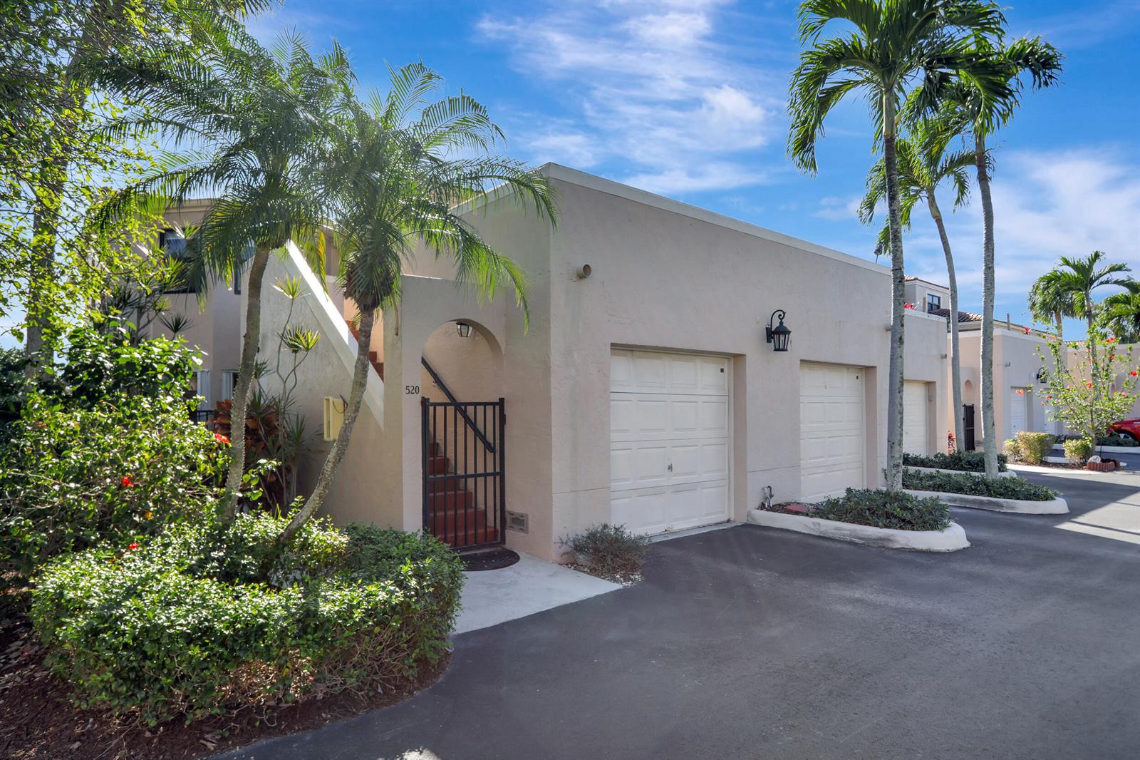 A beige residential building features two garage doors, a gated staircase, and surrounding palm trees — 6646 Villa Sonrisa Drive # 520, Boca Raton FL 33433, BOCA RATON, FL