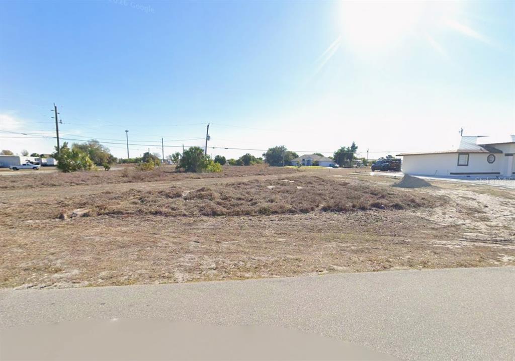 A vacant, grassy lot sits next to a house under a bright, sunny sky — 3148 HIGHLANDS ROAD, PUNTA GORDA, FL