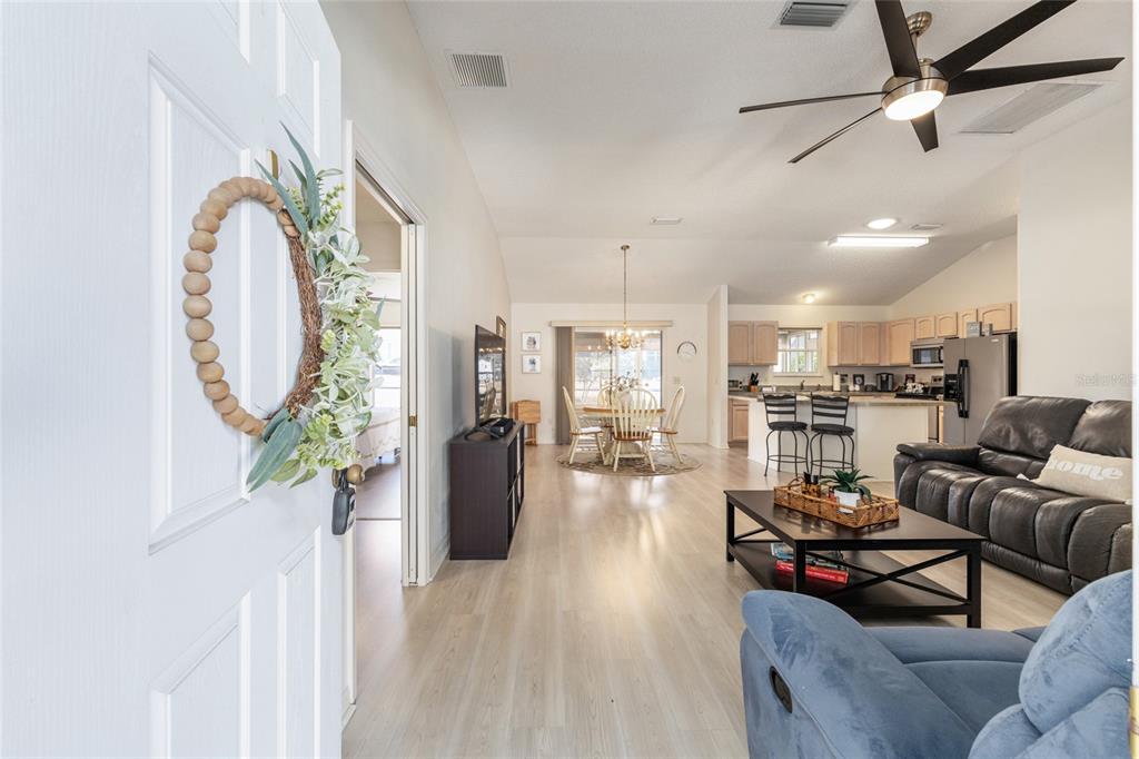 An open-concept living area features light wood flooring, a kitchen with bar seating, and dining — 8337 SE 176TH LAWSON LOOP, THE VILLAGES, FL