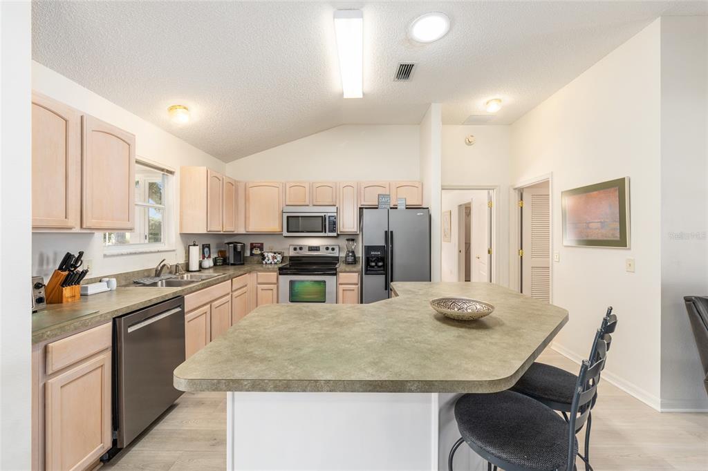 A kitchen features light wood cabinets, a large island with seating, and stainless steel appliances — 8337 SE 176TH LAWSON LOOP, THE VILLAGES, FL