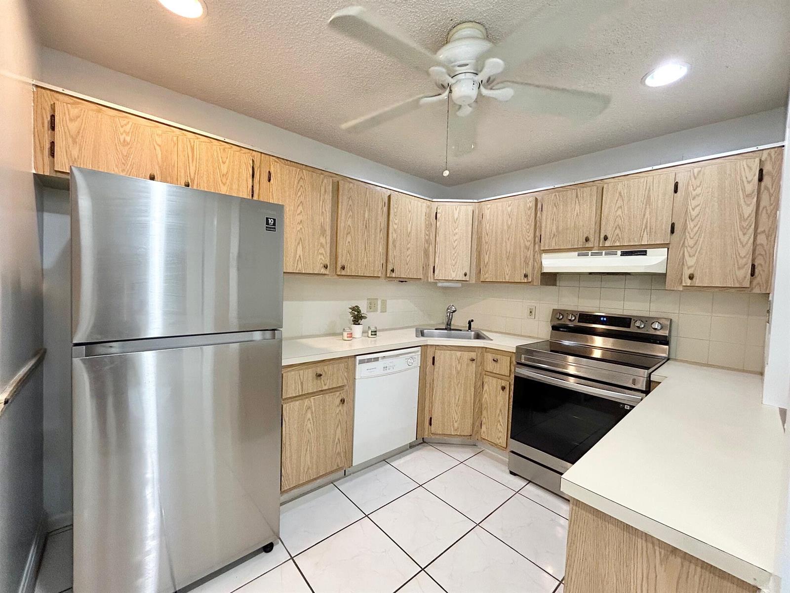 A kitchen features light wood cabinets, stainless steel appliances, white countertops, and white tile flooring — 433 Pine Glen Lane # C2, FL 33463, FL