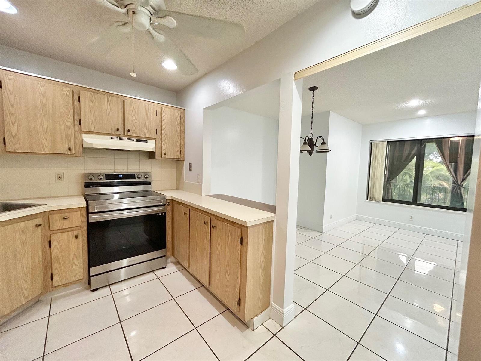 A kitchen with light wood cabinets and white tile floors opens into a dining area — 433 Pine Glen Lane # C2, FL 33463, FL